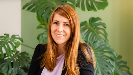 Kathrin Schönborn lächelt in die Kamera und sitzt vor einer großen Pflanze in ihrem Büro