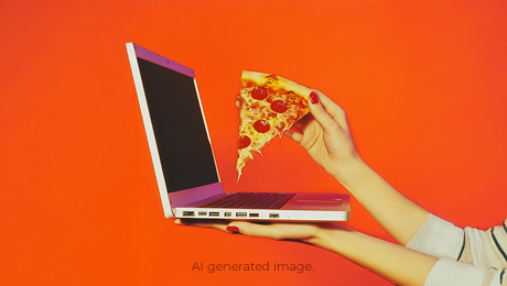 Eine Frau hält einen Laptop und ein Stück Pizza in der Hand