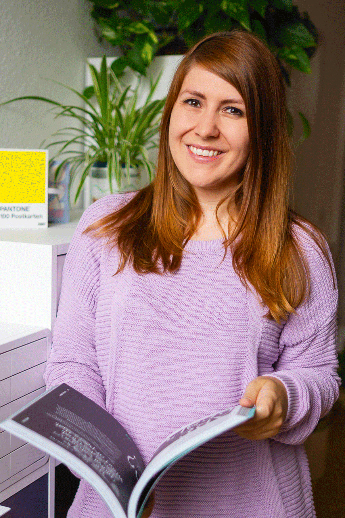 Kathrin Schönborn trägt einen lila Pullover, schaut in die Kamera und steht in ihrem Büro