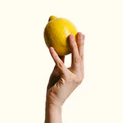 Eine Hand hält eine gelbe Zitrone in die Höhe