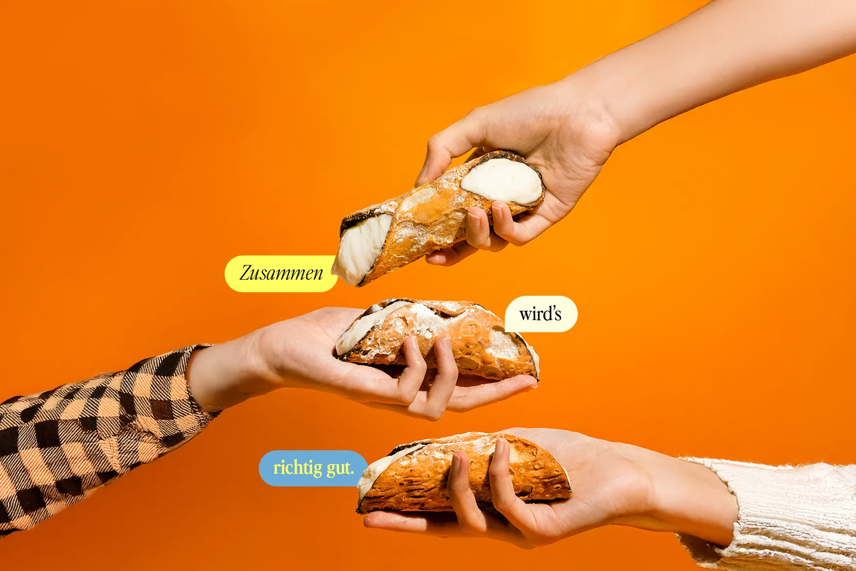 Drei Hände halten gefüllte Cannolos vor einem orangenen Hintergrund in die Höhe